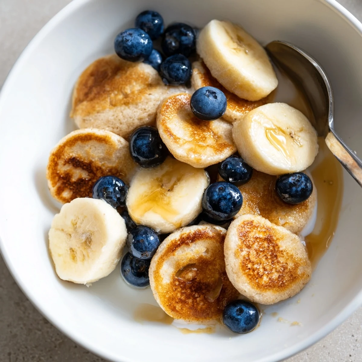 Mini Pancake Cereal served in a bowl with milk and fresh berries, delightfully sweet.  