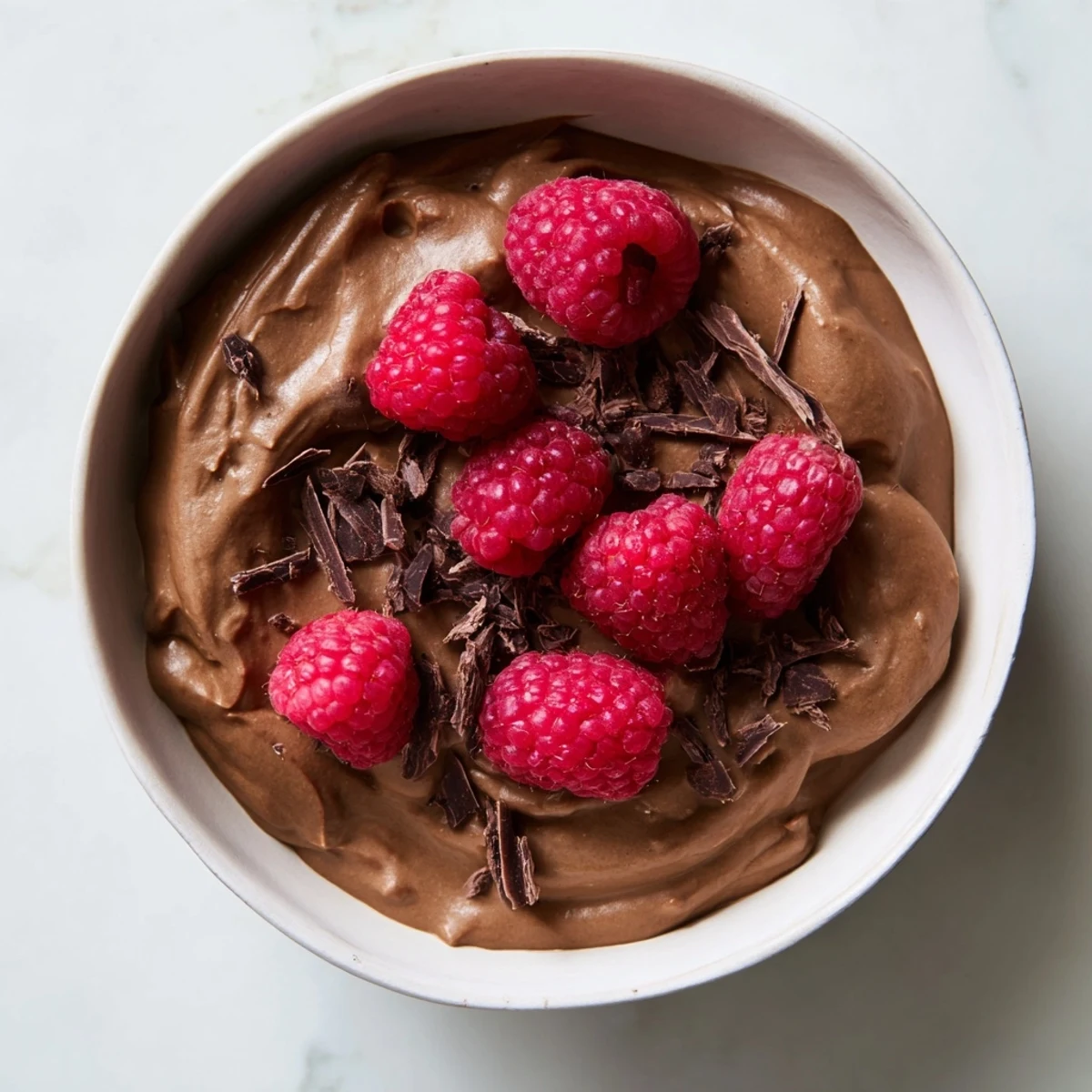 Dark chocolate shaved over creamy avocado chocolate mousse and fresh raspberries for a delicious dessert.