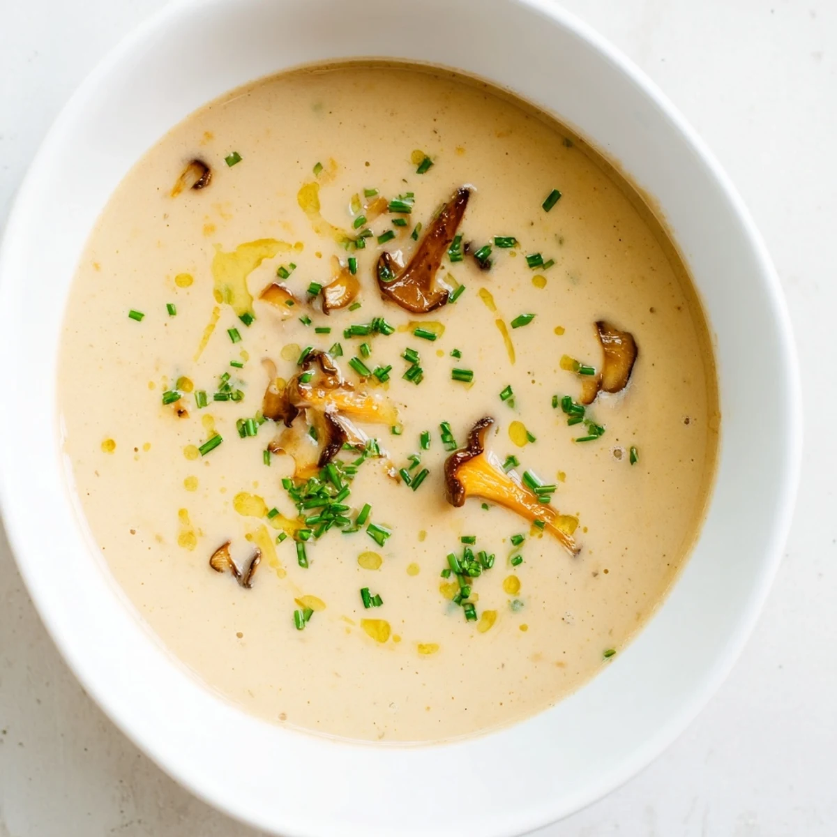 Steaming bowl of creamy mushroom bisque, garnished with fresh chives, ready to eat.