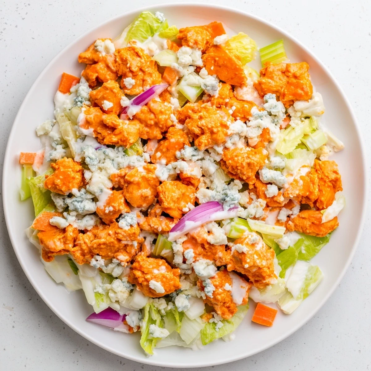 A vibrant bowl of Buffalo Chicken Chopped Salad with shredded carrots and red onion for a crisp, zesty lunch.  