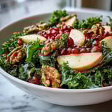The fresh Kale and Pomegranate Bowl showcases a colorful mix of greens, juicy seeds, sliced apple, and a light honey-Dijon dressing glistening.  