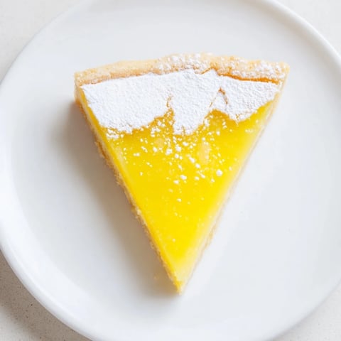 Golden, triangular lemon bars dusted with powdered sugar, ready to eat this refreshing, sweet dessert.