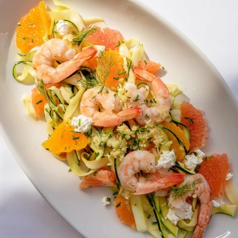 Vibrant The Coral Reef dish features juicy shrimp, citrus segments, and bubbly Gruyère cheese, arranged beautifully.