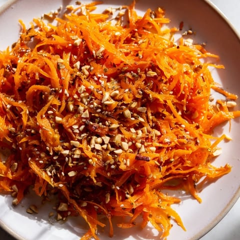 Vibrant Spicy Carrot Salad with shredded carrots, a tangy dressing, and toasted sesame seeds.
