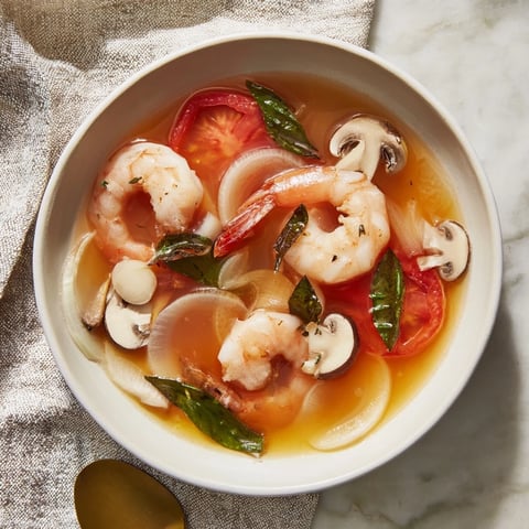 Steaming bowl of Spicy Tom Yum Soup, garnished with fresh cilantro and lime wedges, looks delicious.