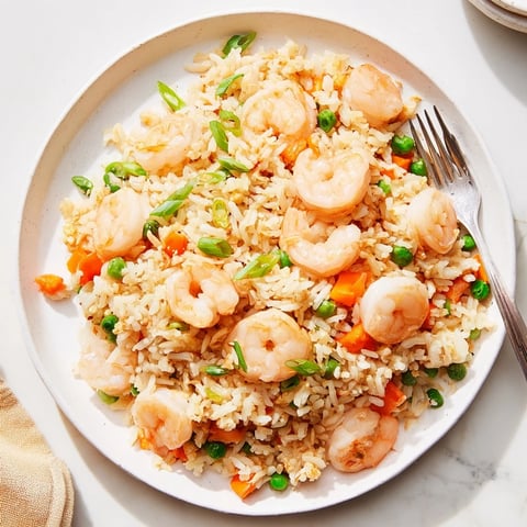 Golden shrimp and fluffy jasmine rice sizzle in a wok with minced garlic, diced carrots, and vibrant peas for a quick, savory meal.