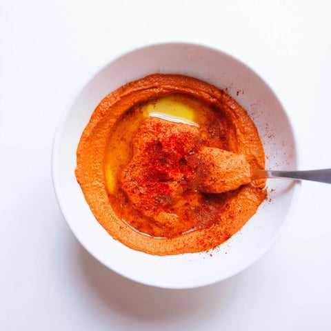 A bowl of homemade Roasted Red Pepper Hummus garnished with olive oil and paprika.