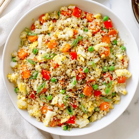 A close-up of vibrant Cauliflower Fried Rice featuring tender riced cauliflower, colorful carrots, peas, and diced red bell pepper.