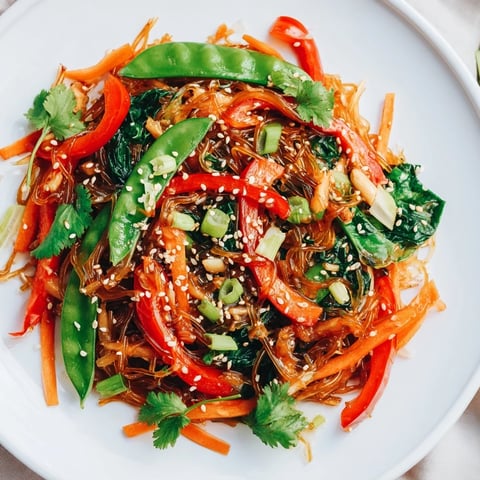 A close-up of kelp noodle stir-fry with vibrant red bell pepper and snap peas glistening in ginger sauce.