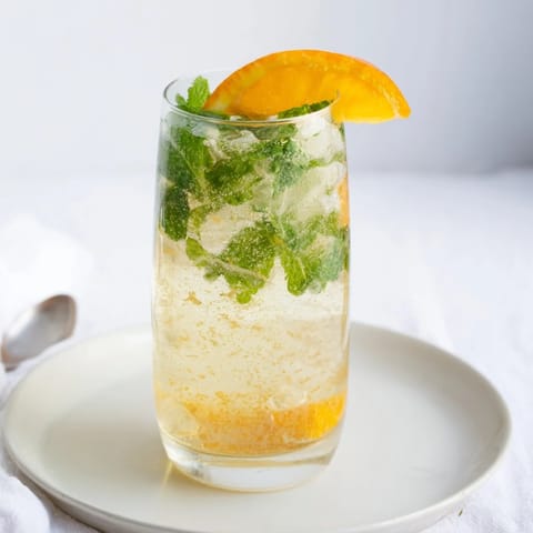 Close-up of a refreshing Probiotic Soda Mocktail garnished with orange slices and mint.  