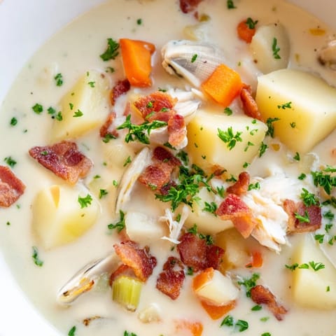 A steaming bowl of New England Clam Chowder, filled with clams and potatoes, sits elegantly beside oyster crackers.