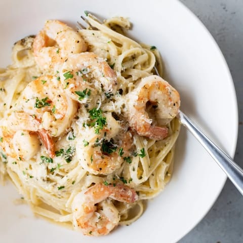 A close-up of Creamy Garlic Shrimp Pasta, garnished with fresh parsley and lemon wedges for a bright finish.