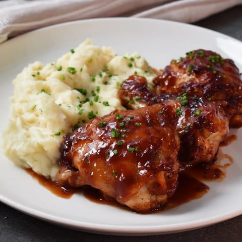 Honey BBQ Chicken Thighs with glistening sauce next to fluffy garlic mashed potatoes, a flavorful plate.