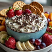 Creamy cottage cheese cookie dough dip with chocolate chips served alongside fresh strawberries and apple slices for a healthy dessert.  