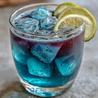 Refreshing butterfly pea flower lemonade with a magical blue-to-purple color change, garnished with lemon slices and ice.